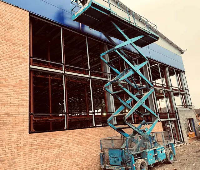 Curtain wall framing being installed into a brick opening from a scissor lift